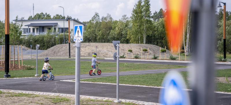 kaksi lasta pyöräilee asfalttiradalla, etualalla liikennemerkki