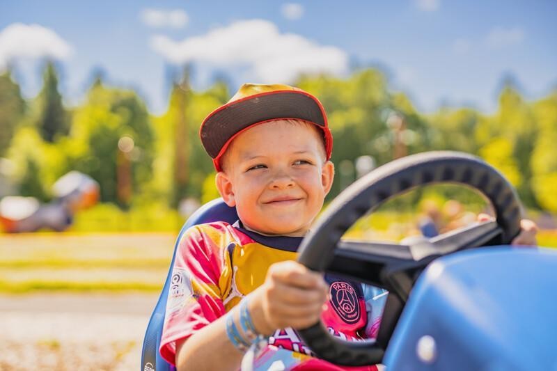 Poika istuu ja hymyilee polkuauton ratissa.