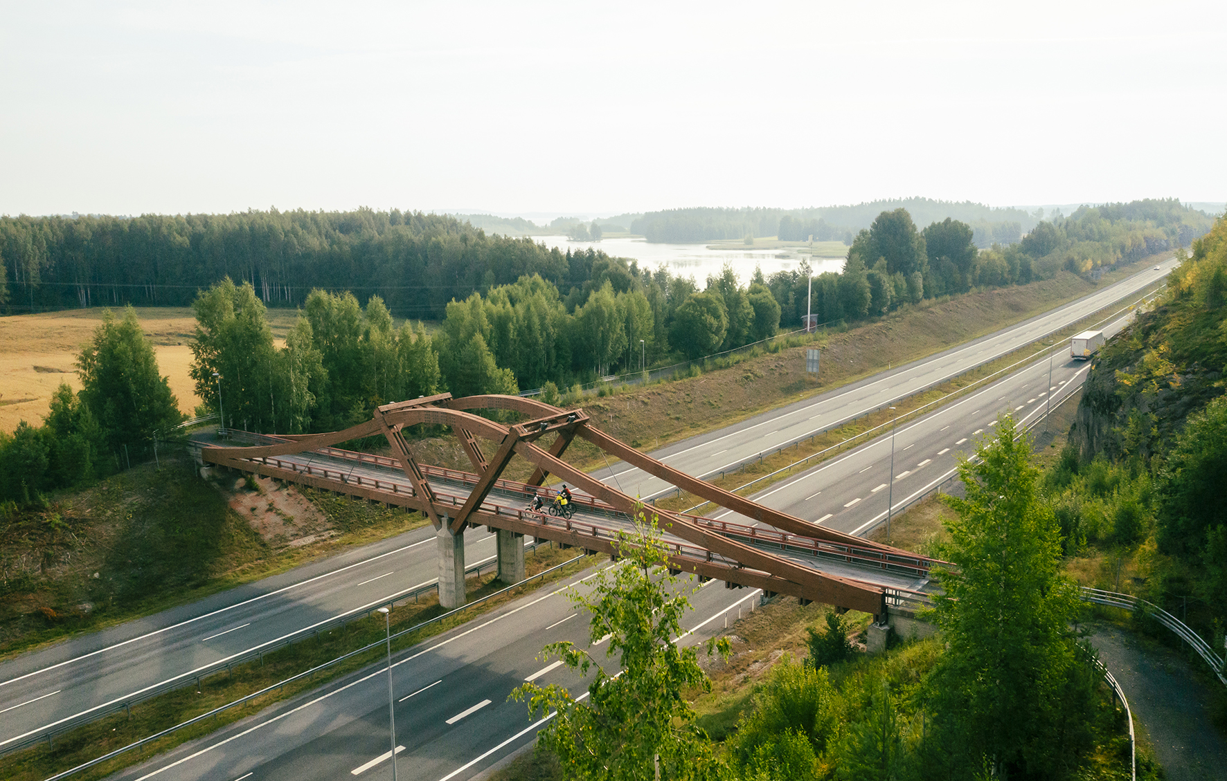 Ilmasta otettu kuva tien yli menevästä sillasta, jolla ajaa pyöräilijöitä.