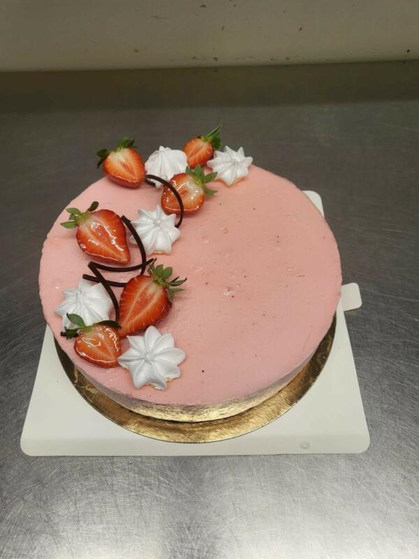 Vaaleanpunainen kakku, joka on koristeltu mansikoilla ja marengilla.