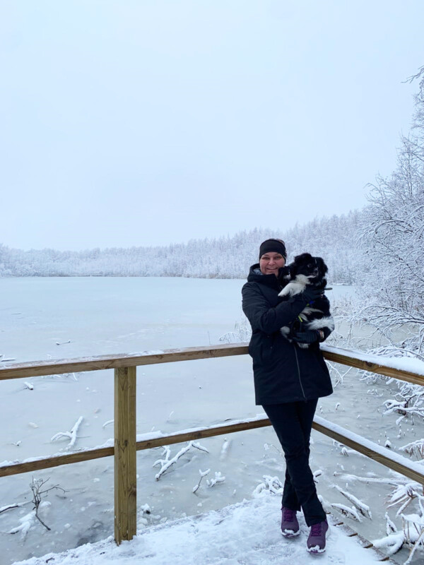 Laura Autio seisoo ulkona talvimaisemassa koira sylissään.